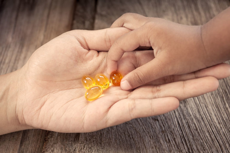 Barnehånd tar vitaminpille fra voksenhånd